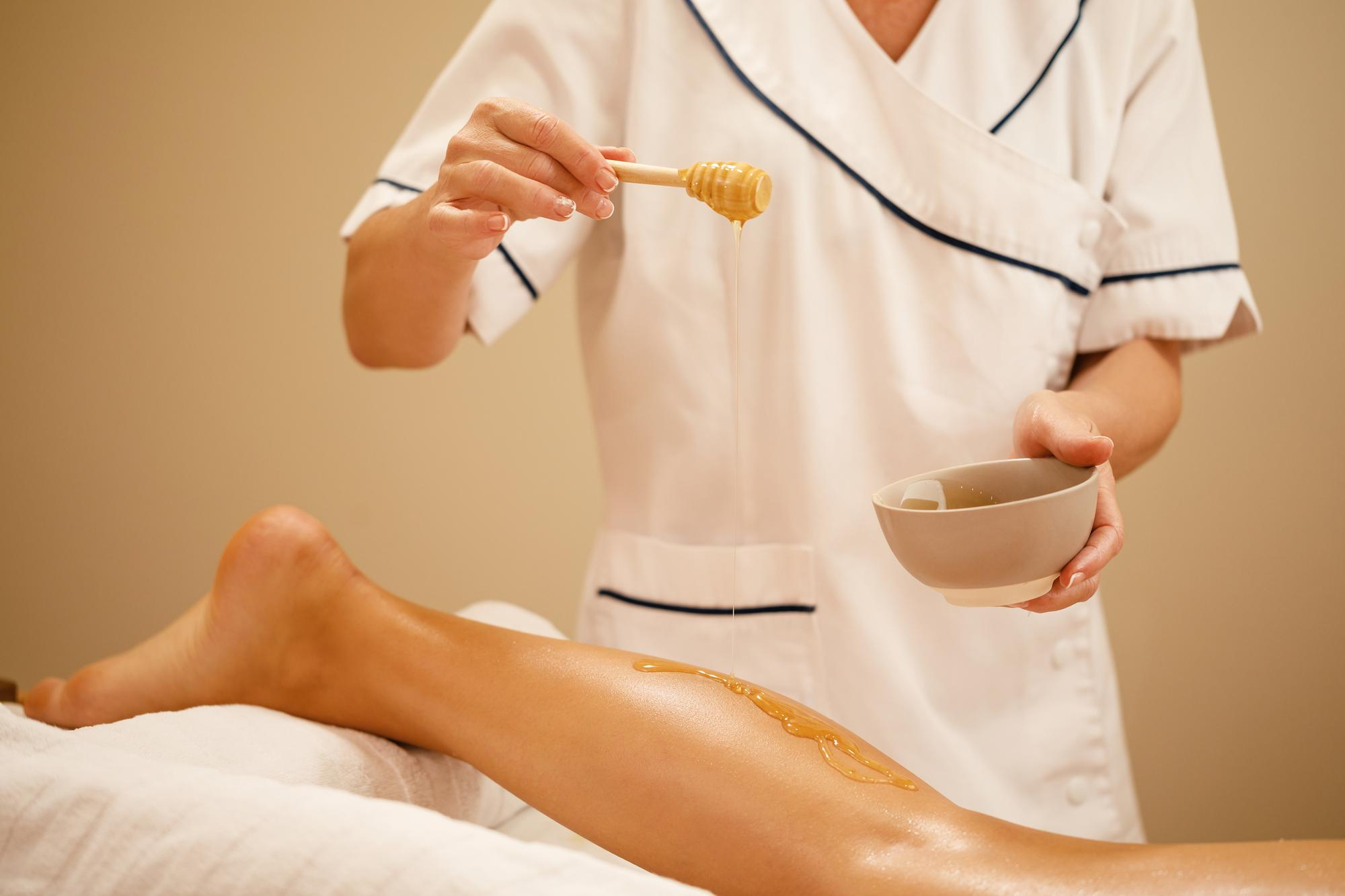 unrecognizable-therapist-pouring-honey-while-massaging-woman-s-leg-spa-salon